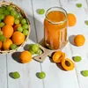 A collection of apricots and grapes are arranged around a jar of jam on a wooden surface. Produktbild-Vorschau