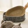 A cat is lying on the floor next to a cat bed with a scratching board insert. Produktbild-Vorschau