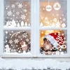 A child wearing a Santa hat looks out a window decorated with Christmas-themed window stickers. Produktbild-Vorschau