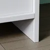 A close-up view of the bottom corner of a white furniture item, possibly a nightstand, resting on a wooden floor. Produktbild-Vorschau