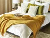A neatly made bed with a mustard yellow throw blanket draped over it, several decorative pillows, and a small tray with a cup and saucer. Produktbild-Vorschau