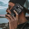 A person holding a black phone case with a stand, outdoors near a body of water. Produktbild-Vorschau