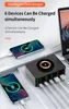 A black multi-port USB charging hub with a wireless charging pad on top, connected to several smartphones and a laptop. Produktbild-Vorschau