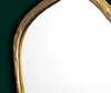 A close-up view of the textured gold frame of an asymmetrical mirror against a dark green background. Podgląd zdjęcia produktu