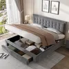 A grey upholstered bed frame with the mattress lifted to reveal storage compartments and drawers underneath. The bed is made with bedding and is in a bedroom setting with a window and artwork on the wall. Produktbild-Vorschau