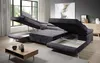 A modern living room with a large, dark gray sectional sofa with storage compartments open, a coffee table, and a large window with greenery outside. Produktbild-Vorschau