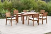 A wooden dining set with chairs and a table on a patio, surrounded by greenery and flowers. Produktbild-Vorschau