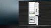 An open refrigerator with its interior shelves and drawers visible, set against a dark, textured background. Produktbild-Vorschau