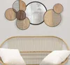 A wall mirror with a decorative wooden frame is mounted on a light gray wall above a rattan sofa with white cushions. Produktbild-Vorschau