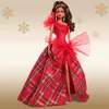 A Barbie doll wearing a red plaid gown, standing against a gold background with snowflakes. Náhľad obrázku produktu