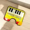 A yellow piano-shaped bath mat with flame accents is shown on a wooden surface. Anteprima dell’immagine prodotto