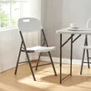A white folding chair is shown in front of a window with natural light. Podgląd zdjęcia produktu