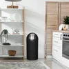 A black trash can with a silver lid is placed next to a white shelving unit in a kitchen or dining area. Produktbild-Vorschau