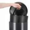 A hand is lifting the lid of a black trash can. Podgląd zdjęcia produktu