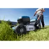A person is using a cordless lawnmower on a grassy lawn on a sunny day. Voir les images du produit