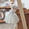 A close-up view of a toy doll's pram made of wicker, with a wooden handle and a tassel detail. Produktbild-Vorschau