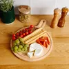 A wooden serving board with cheese, grapes, cherry tomatoes, breadsticks, and small sausages. Produktbild-Vorschau