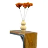 A vase with artificial flowers sits on a wooden table. Voir les images du produit