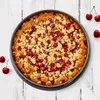A cherry crumble cake in a springform pan, placed on a white wooden surface with a few cherries scattered around. Anteprima dell’immagine prodotto