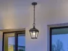 An outdoor pendant light fixture hangs from a chain against a light-colored wall, with windows visible on either side. Produktbild-Vorschau