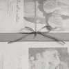 A close-up of a gray ribbon tied into a bow on a patterned fabric. Produktbild-Vorschau