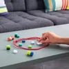 A hand is playing with a magnetic game on a table, with a couch in the background. Voir les images du produit