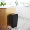 A black trash can with a gold lid sits next to a gold kitchen island in a modern kitchen. Produktbild-Vorschau