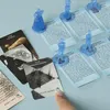 A close-up view of a board game setup, featuring blue character pawns and game cards on a light blue surface. Produktbild-Vorschau