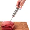 A hand is holding a stainless steel meat injector and inserting it into a piece of raw red meat on a wooden cutting board. Voir les images du produit
