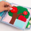 A hand is shown interacting with a felt quiet book page featuring a tree with apples. Produktbild-Vorschau
