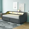 A dark gray upholstered daybed with a built-in shelf featuring LED lighting and a tablet is shown in a room with light blue walls and a patterned rug. Produktbild-Vorschau