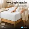 A person sitting on a bed with a white fitted sheet. Produktbild-Vorschau