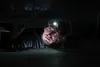 A person wearing a headlamp is working in a dark, confined space. Produktbild-Vorschau