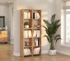 A modern wooden bookshelf filled with books and decorative items, placed in a bright room with a large window and a potted plant. Produktbild-Vorschau
