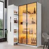 A white display cabinet with glass doors and internal LED lighting, showcasing bottles and other items. A pull-out cabinet is visible on the left. Produktbild-Vorschau