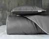 A folded duvet and a pillow with gray fabric and white trim, against a textured gray wall and a white surface. Náhled obrázku produktu