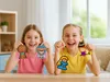 Two young girls are smiling and holding up handmade bead figures. Produktbild-Vorschau