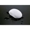 A white, oval-shaped object with water droplets on it, resting on a reflective black surface with scattered water droplets. Produktbild-Vorschau
