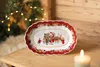 A festive Christmas scene with a decorated oval dish on a wooden table, a Christmas tree with lights in the background, and a lit candle in the foreground. Produktbild-Vorschau