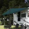 An RV awning provides shade over two chairs and a storage box in a grassy, wooded area. Náhled obrázku produktu