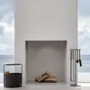 A modern fireplace set with tools and a log holder, set against a backdrop of a window overlooking the sea. Anteprima dell’immagine prodotto
