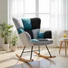A patchwork rocking chair is placed in a bright room with a window and plants. Produktbild-Vorschau
