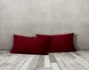 Two burgundy pillows are placed on a wooden floor in front of a textured gray wall. Produktbild-Vorschau