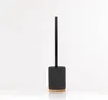 A toilet brush with a black ribbed holder and a wooden base, standing upright against a white background. Anteprima dell’immagine prodotto