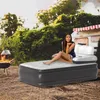 A woman is sitting on an inflatable mattress outdoors, with a campfire and a camper van in the background. Náhled obrázku produktu