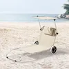 A beige beach lounger with wheels and a canopy sits on a sandy beach with the ocean in the background. Náhled obrázku produktu