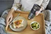 A person holding a travel mug over a tray with toast and grapes. Podgląd zdjęcia produktu