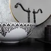 A close-up view of a decorative washbasin with faucets and a mirror in the background. Náhled obrázku produktu