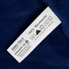 A close-up of a clothing care label attached to a dark blue fabric. Produktbild-Vorschau