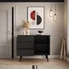 A modern living room scene featuring a black and wood sideboard with drawers and open shelving, decorated with a vase of dried flowers and a framed abstract artwork. Produktbild-Vorschau